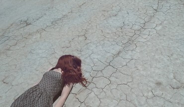 Dziewczyna lezy na spękanej, pustynnej ziemi
